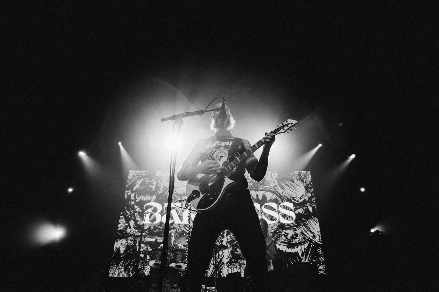 Baroness guitarist backlit at the mic before the band's logo screen and beams of stage light, The Palace Theatre, Calgary