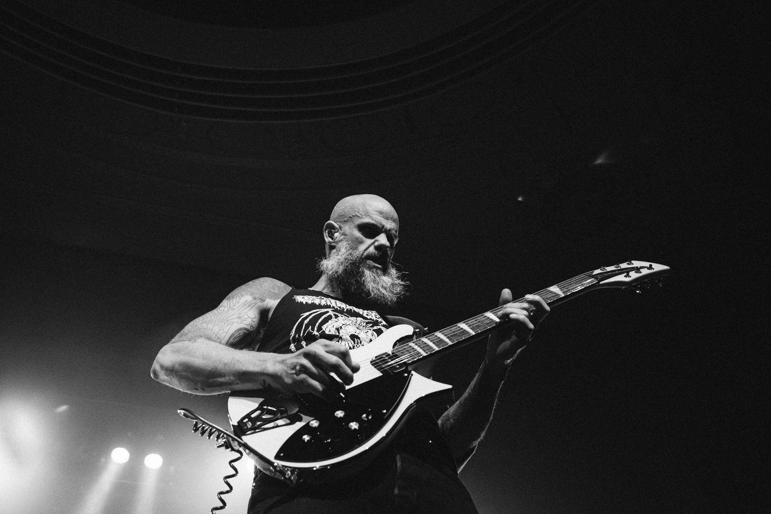 Bearded, bald Baroness guitarist plays a white and black guitar, shot from below at The Palace Theatre, black and white