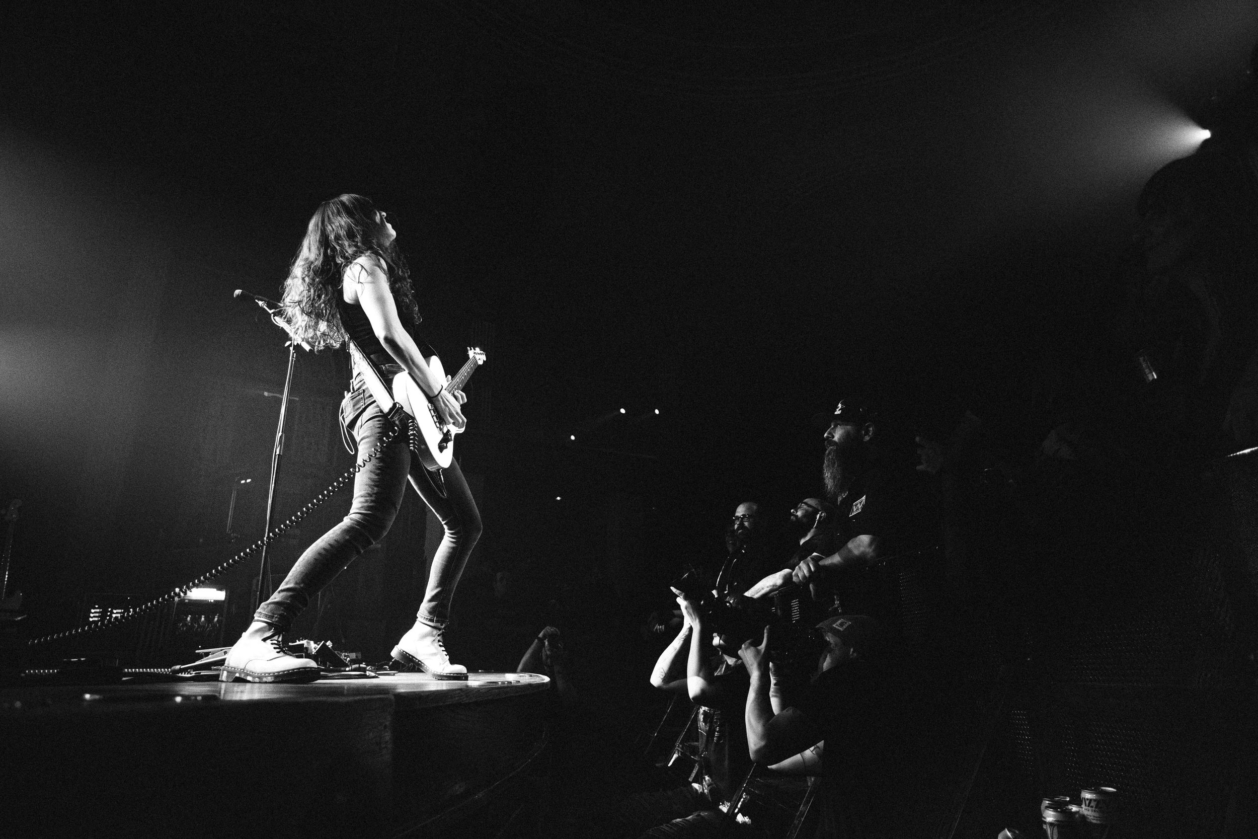 Long-haired Baroness guitarist plays at the stage edge above a cheering crowd at The Palace Theatre, Calgary, black and white