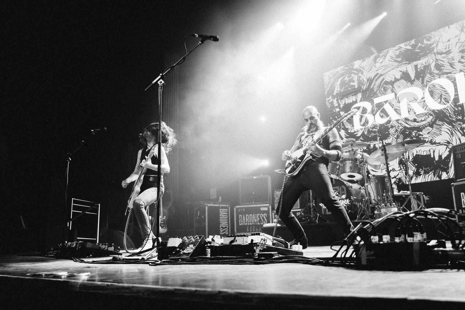 Two Baroness guitarists play through haze and light beams on stage at The Palace Theatre in Calgary, black and white