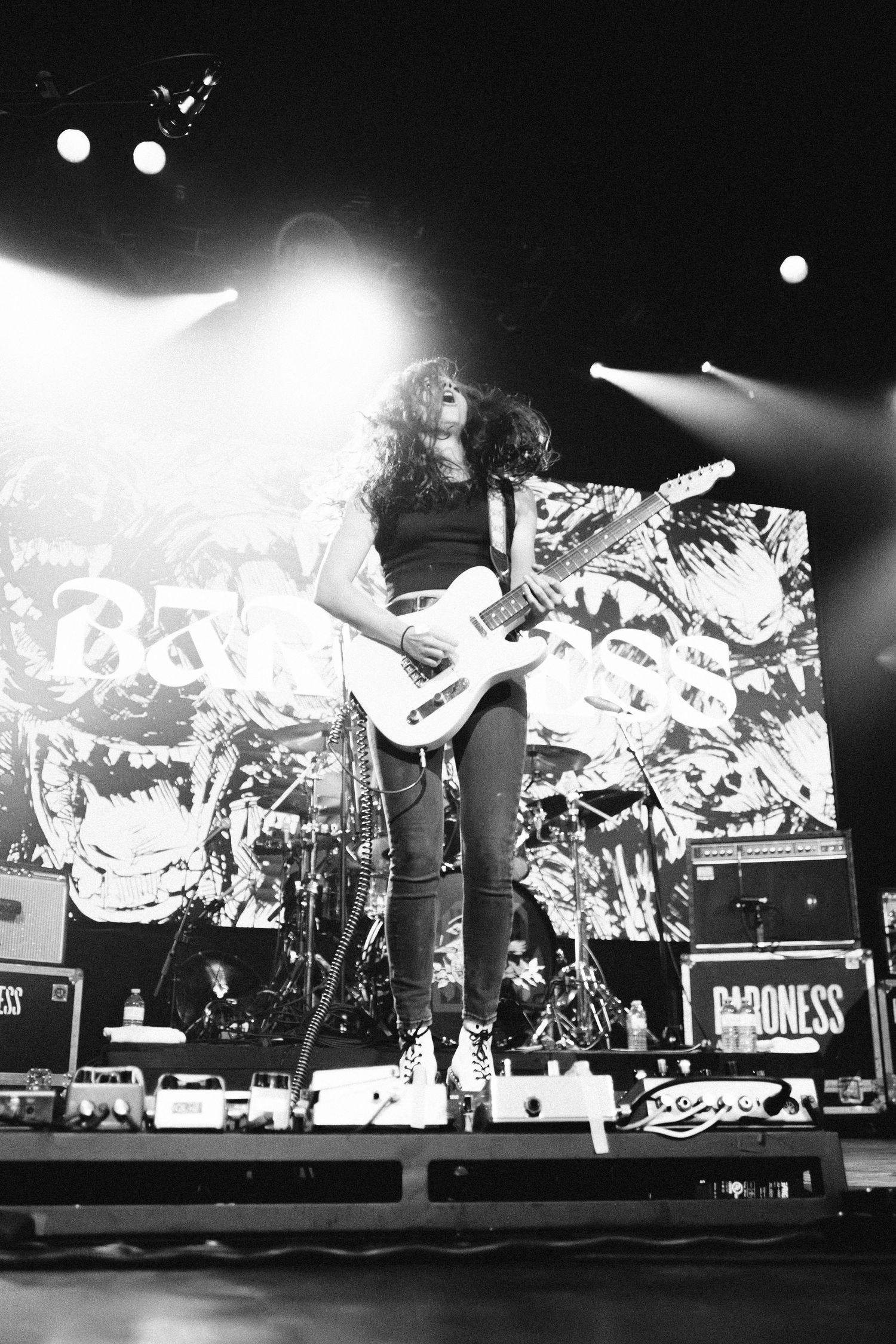 Low-angle view of a long-haired Baroness guitarist on a white guitar before the logo backdrop, The Palace Theatre, Calgary