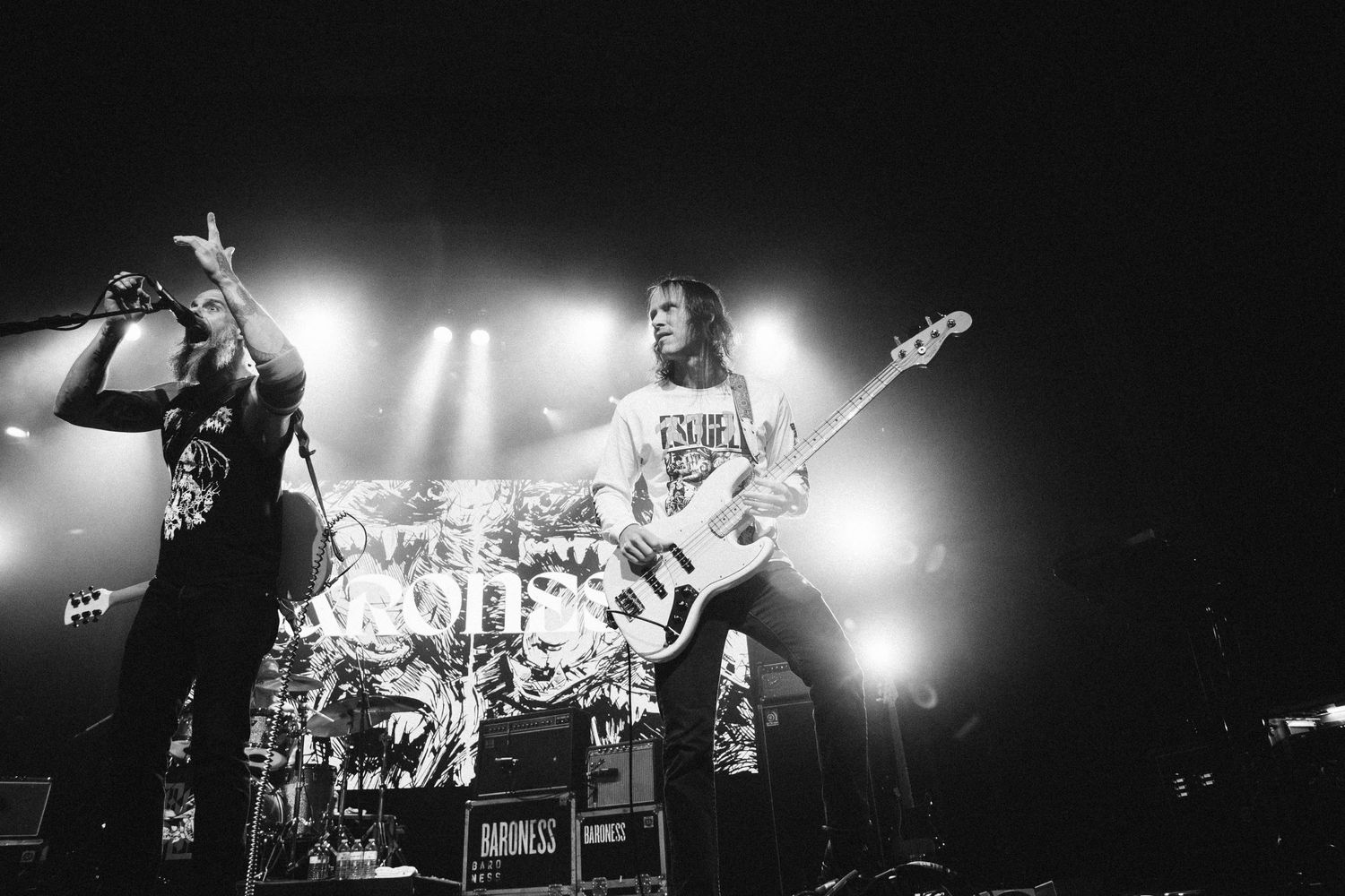 Baroness singer points skyward at the mic beside the bassist, both backlit, The Palace Theatre, Calgary, black and white