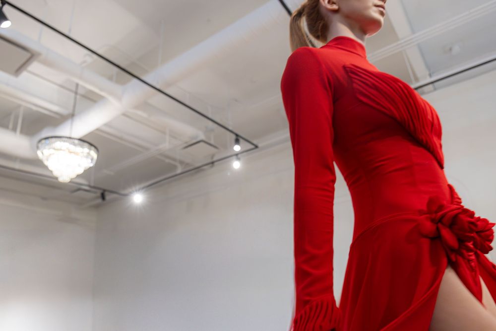 Low-angle view of a model in a fitted red gown with rosette and thigh slit under a chandelier, Edmonton Fashion Week