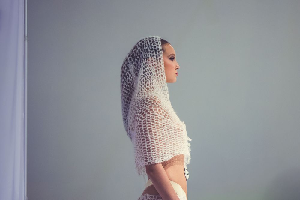Model in profile wearing a white open-knit crochet hood and cropped top on the runway at Edmonton Fashion Week