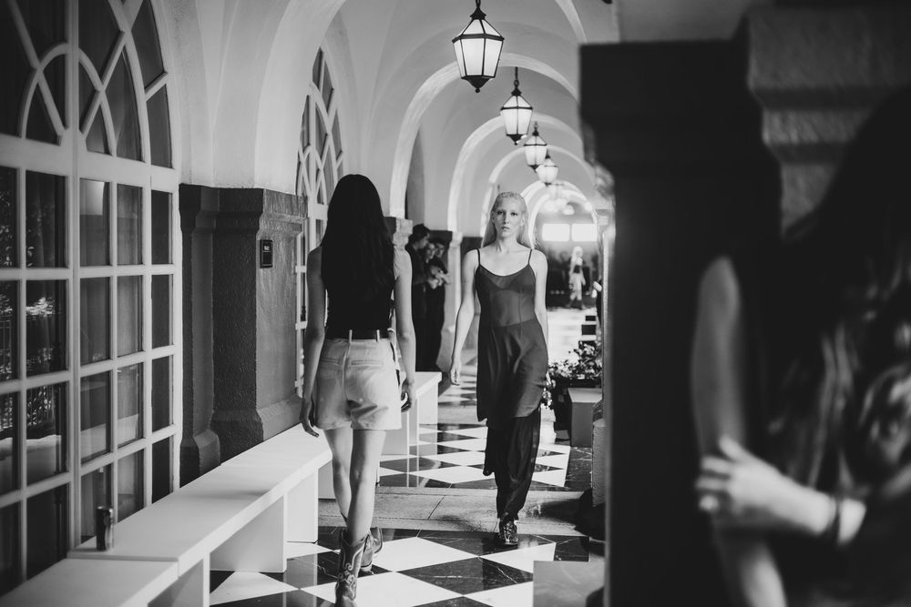 Black and white image of models walking a lantern-lit arched hallway with a checkered floor, Mexico City Fashion Week