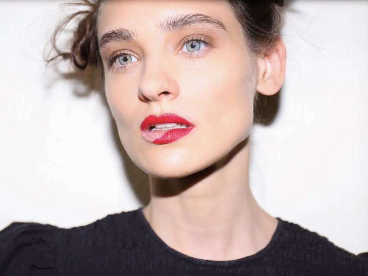 Close-up of a model with blue eyes, loose updo and a half-painted red lip, backstage at Mexico City Fashion Week
