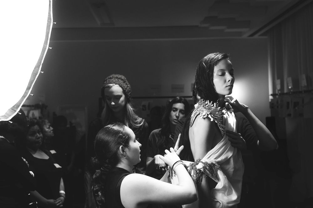 Black and white backstage scene at Mexico City Fashion Week: a dresser adjusts a model's draped, embellished gown