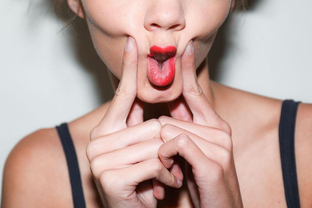 Model with red lipstick pulling her cheeks in a playful pout, backstage makeup by MAC Cosmetics, Mexico City Fashion Week
