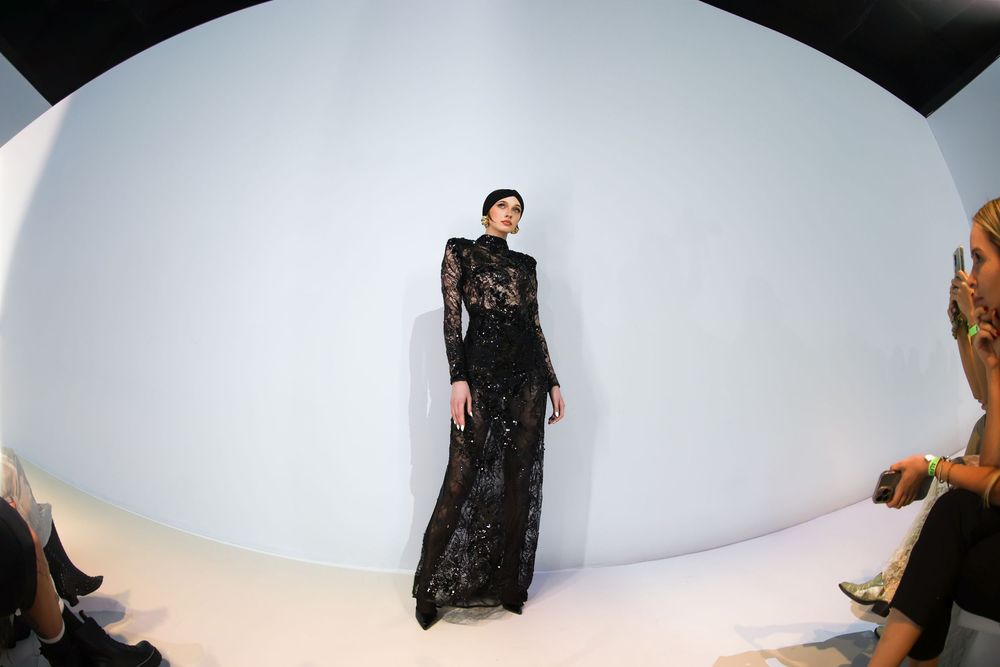 Runway model in a sheer black embellished long-sleeve gown on a curved white set at Mexico City Fashion Week