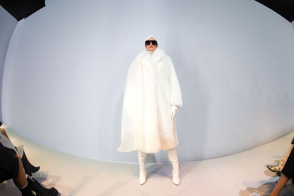 Runway model in an oversized white faux fur coat, hood, sunglasses and white boots at Mexico City Fashion Week