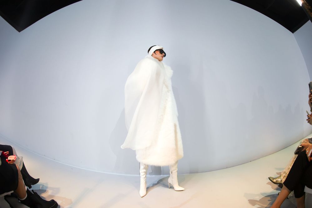 Runway model in a white sheer cape, white visor and white heeled boots on a curved white set, Mexico City Fashion Week