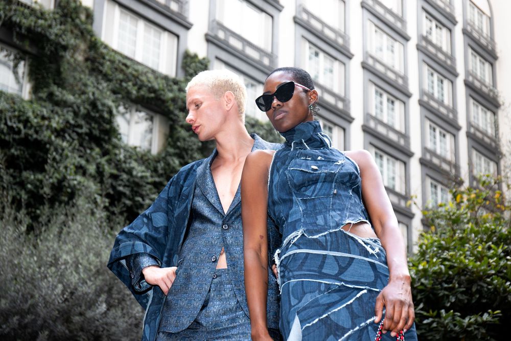 Two models in patchwork denim looks, one in black sunglasses, outside an ivy-covered building at Mexico City Fashion Week
