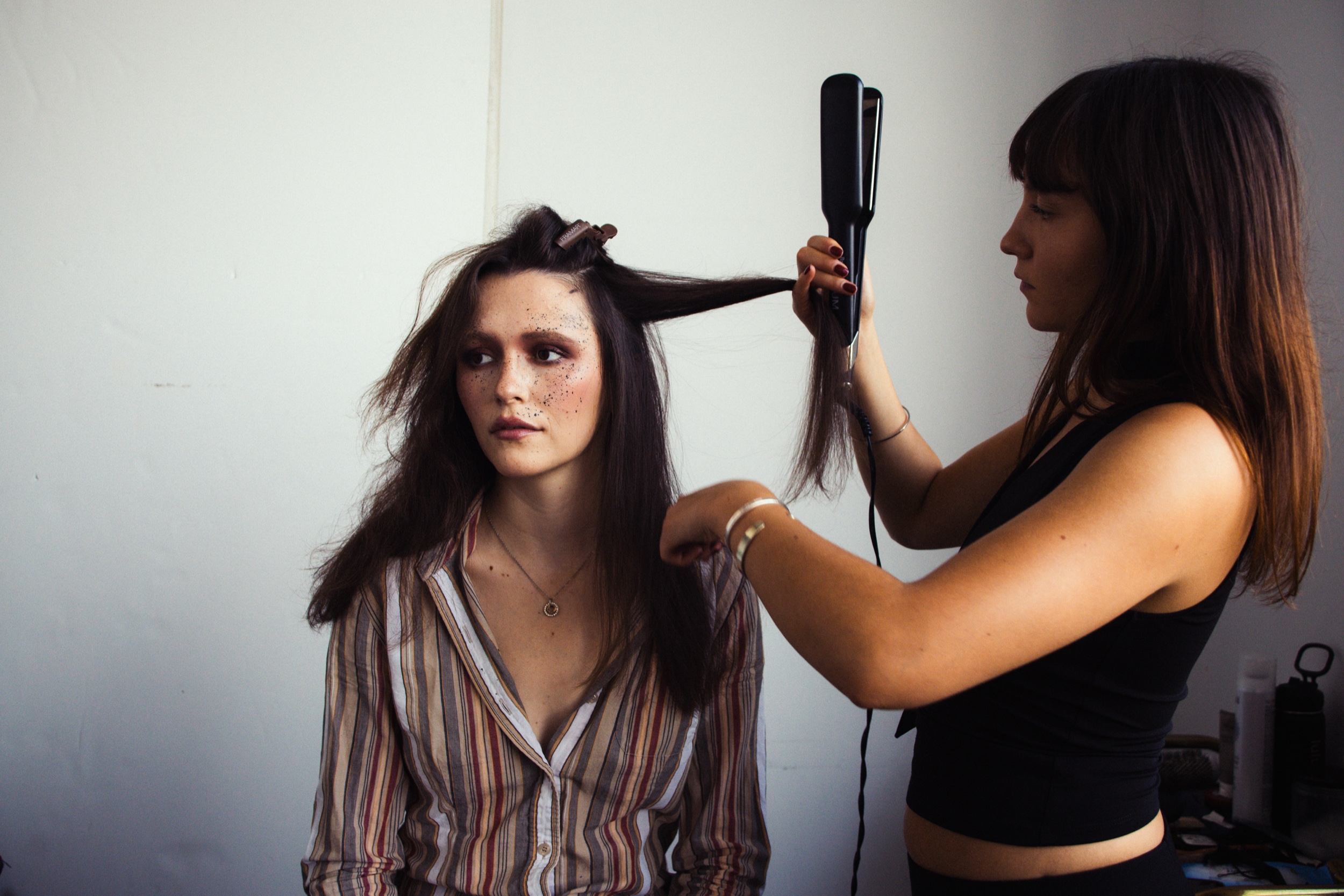 Hairstylist uses a flat iron on a model in a striped shirt backstage, Montreal Fashion Week 2025